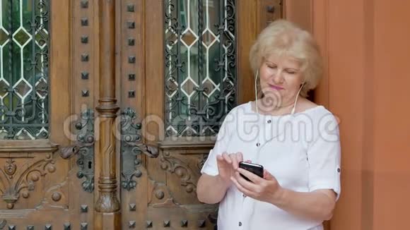 使用带有耳机的智能手机的老年妇女背景中的老式建筑视频的预览图