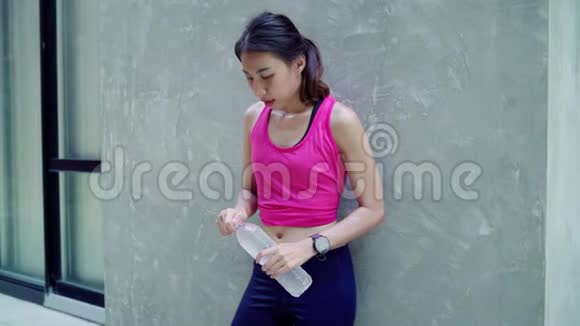慢动作健康美丽的年轻亚洲跑步女子饮水因为在城市街头跑步后感到疲倦视频的预览图