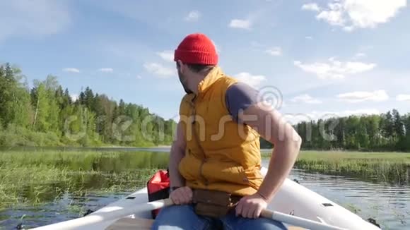 年轻的混合种族白种人留胡子的希普斯特男子划船充气船与木桨在湖上HD慢动作生活方式视频的预览图
