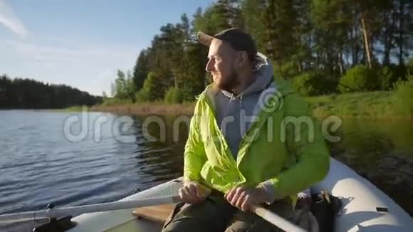 年轻的微笑快乐男子划船充气船与木桨在湖上高清慢动作生活方式录像视频的预览图