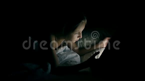 年轻快乐的白种人女孩晚上躺在床上看平板电脑上的电影视频的预览图