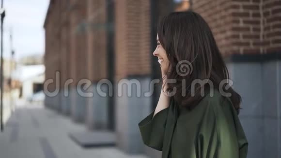 可爱的女孩穿着绿色衬衫在街上打电话侧视视频的预览图