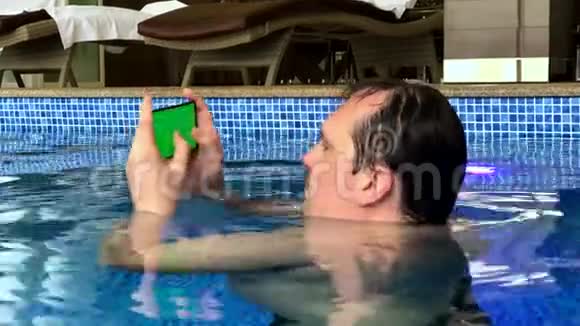 在泳池里使用智能手机的中年男人视频的预览图