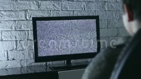 小男孩看液晶电视在一个黑暗的房间与阁楼风格砖墙背面视图视频的预览图