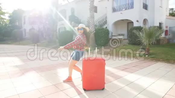 带着红手提箱到达度假胜地或公寓的快乐年轻女子视频的预览图