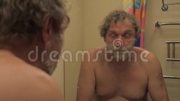 一个英俊的成年男子看着镜子刮胡子视频的预览图