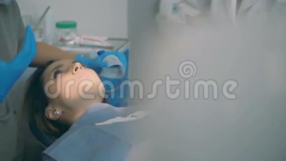 年轻女子躺在牙科椅上听医生说话牙医和牙科护士建议病人视频的预览图