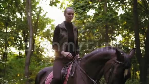 阳光明媚的一天小女孩在公园里骑着漂亮的棕色马美丽的女骑手坐在马鞍上视频的预览图