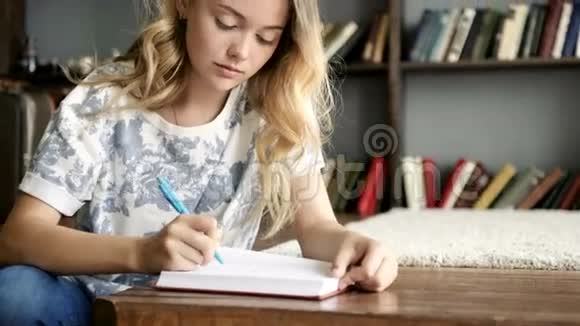 年轻漂亮的女孩在学校的笔记本上写着一封信看着相机视频的预览图