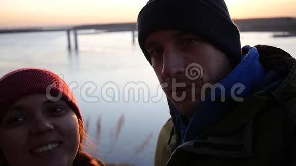 年轻夫妇正在电话里拍照在河边的夕阳背景下笑着看着摄像机视频的预览图