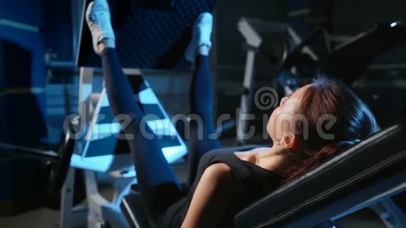 那个女孩正在健身房训练腿按在模拟器中用于大腿和臀部的背部4k视频的预览图