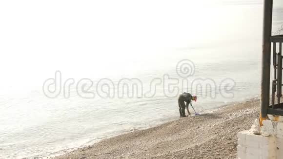 一个拿着金属探测器的人正在海滩上寻找有价值的物品黎明时分雾中视频的预览图