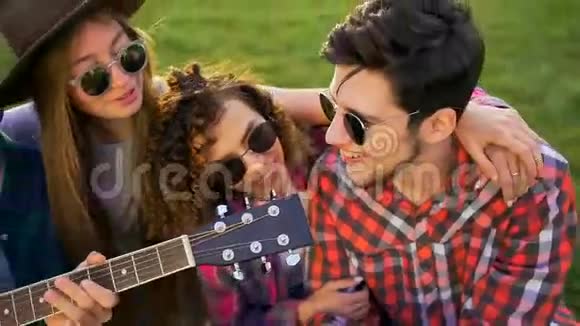 四个朋友正在拥抱弹吉他在日落时在户外唱歌他们很高兴很高兴视频的预览图