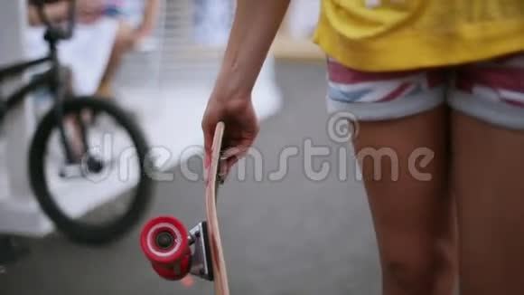 穿短裤的年轻女人手里拿着红色的轮子扭曲滑板夏日之夜明亮的指甲视频的预览图