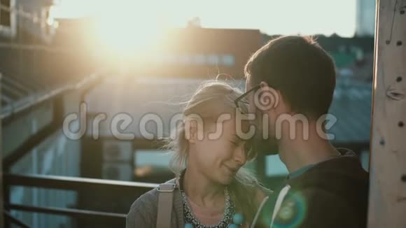 年轻漂亮的夫妇站在阳台上在日落时拥抱在浪漫的约会中快乐的男人和女人视频的预览图