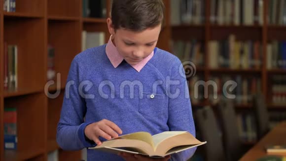 一张可爱的小学生的肖像站在图书馆的书架旁读着一本书视频的预览图