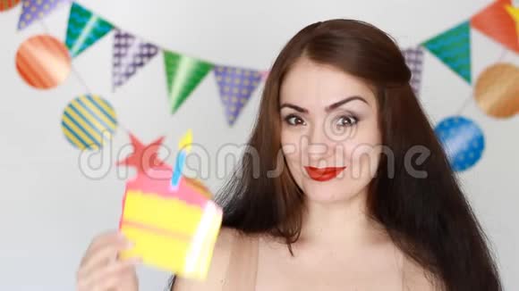 那个有趣的女孩微笑着手里拿着蛋糕吹出一支纸烛年轻快乐女人特写的肖像视频的预览图