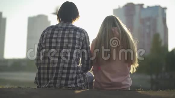 男人和女孩坐在河岸上看着这座城市视频的预览图