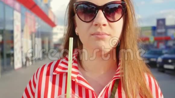 夏天穿红色衣服的年轻女孩的肖像女孩从稻草中喝酒近距离射击视频的预览图