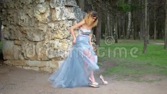 穿着银色和蓝色连衣裙的漂亮女孩穿上高跟鞋准备在石堆附近拍照时摆姿势视频的预览图