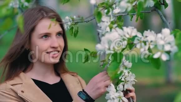 美丽的年轻女子在春天的苹果园享受大自然快乐的美丽女孩在花园里盛开的树香气视频的预览图
