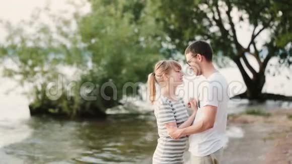年轻漂亮的男人和女人站在海滩上说话幸福的一对夫妇拥抱在河岸上视频的预览图