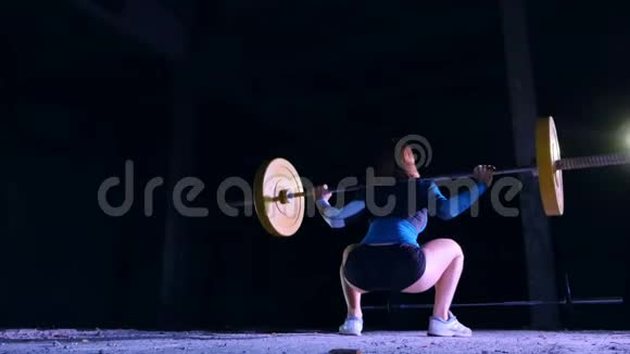运动的年轻女子举起杠铃用杠铃做仰卧起坐后景在夜晚在视频的预览图