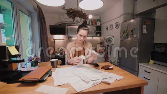 年轻女子坐在厨房的桌子旁在购物后计算账单家庭账户部视频的预览图
