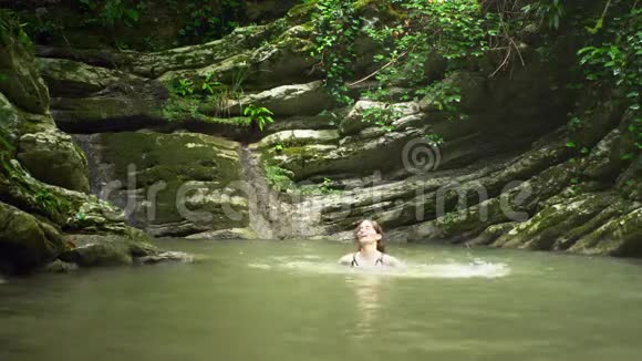 年轻女子在绿色热带森林的小湖里洗澡视频的预览图