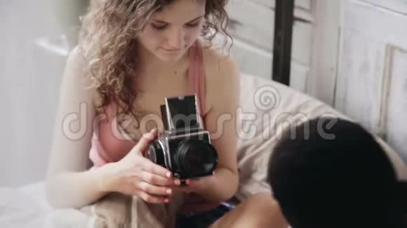 摄影师在旧的移动胶卷相机上拍照穿睡衣的年轻女人拍照透过窗帘看视频的预览图