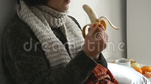 穿毛衣的生病的年轻女人躺在床上吃香蕉视频的预览图