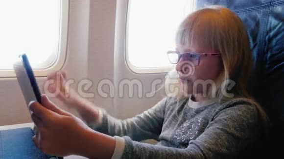 一个戴眼镜6年的女孩坐飞机旅行在飞行中使用数码平板电脑视频的预览图