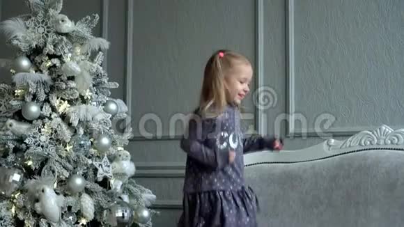 这个金发小女孩在圣诞树上的沙发上玩尾巴可爱的女孩在装饰的附近玩耍视频的预览图