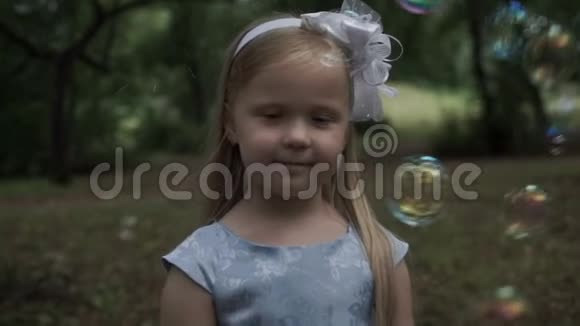 在公园里一个肥皂泡背景下美丽的小女孩视频的预览图