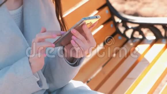 女人坐在公园的长凳上在手机里输入一条信息特写双手视频的预览图