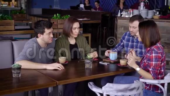 四个朋友坐在咖啡馆的桌子旁享受着他们的晚餐互相交谈两对情侣聊天视频的预览图
