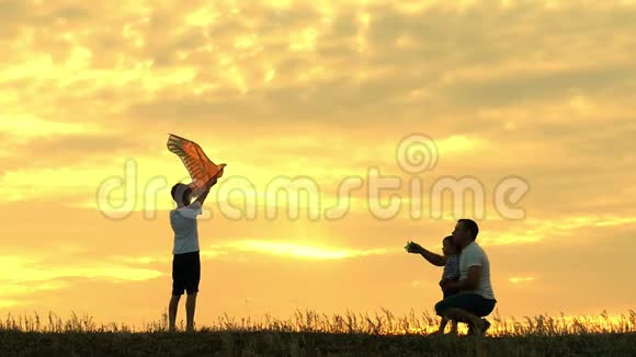 快乐的父亲家人和孩子在夏天的日落时缓慢地跑进风筝的天空家庭户外视频的预览图