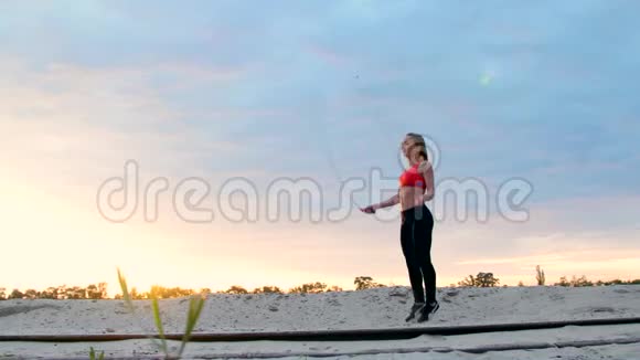 美丽苗条的年轻女子从事健身跳绳黎明时在一个货鹤附近在沙石场视频的预览图