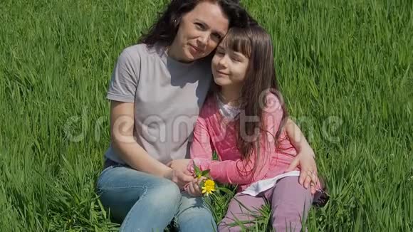 妈妈在绿色的草坪上拥抱女儿公园里有个孩子的女人坐在草地上夏天的家庭视频的预览图
