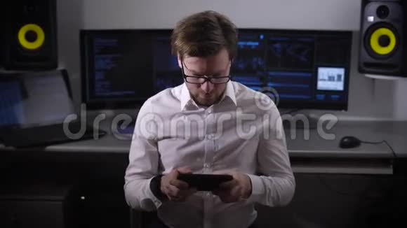 年轻的游戏开发商穿着白色衬衫和黑色裤子坐在办公室里手里拿着平板电脑正在测试视频的预览图