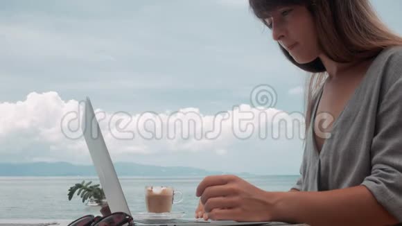 年轻女子在户外咖啡馆的笔记本电脑上工作移动相机稳定器镜头视频的预览图