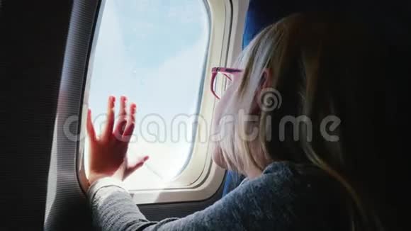 一个戴眼镜的6岁女孩坐在飞机上看着窗外她的手被压在舷窗上很高兴视频的预览图