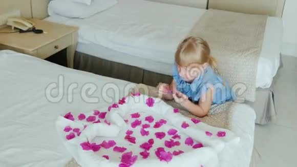 一个手上戴着酒店手镯的6岁女孩正在玩花瓣在她的床上有一个毛巾心视频的预览图