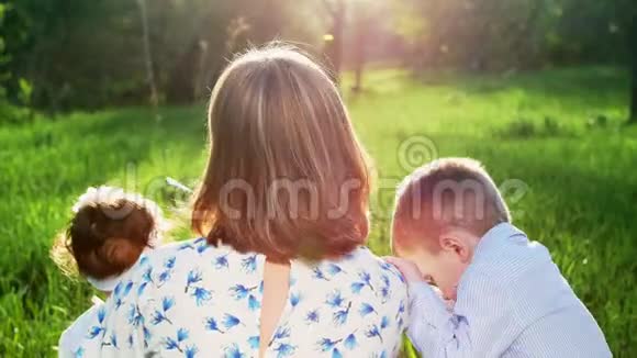 在阳光下在夕阳下在公园的夏天一个年轻的母亲一个金发女人吹着视频的预览图
