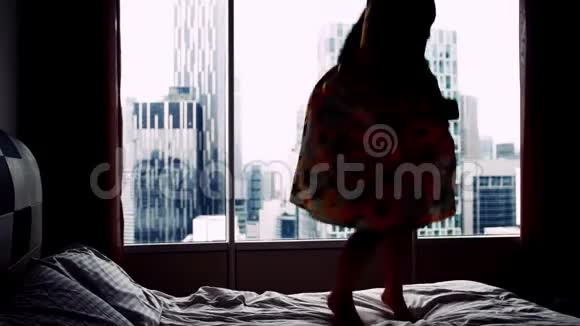 年轻兴奋的女人穿着裙子跳舞跳在酒店床上的背景建筑上的剪影视频的预览图