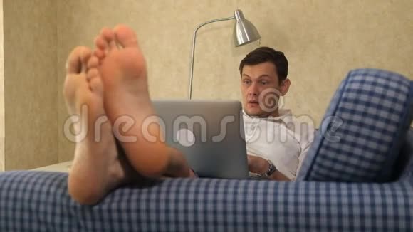 严肃的商人躺在沙发上用笔记本电脑工作沉思脚特写视频的预览图