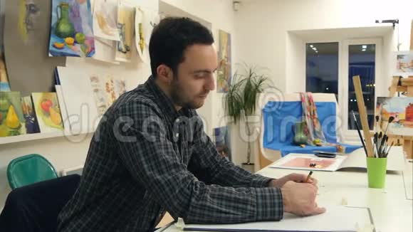 男艺术系学生用铅笔在画室的书桌前做素描视频的预览图