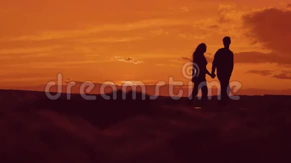 日落时分一对夫妇在海滩上牵手散步的剪影在夕阳的灯光下在海滨快乐的男人和女孩视频的预览图