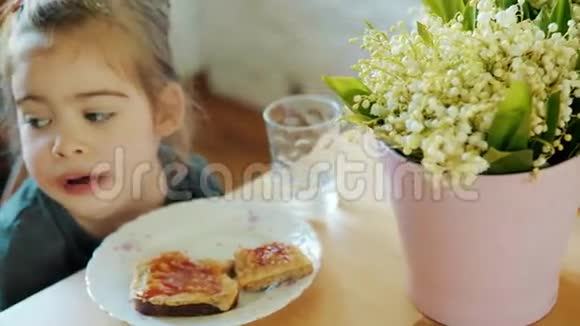 可爱的女孩在餐桌上吃早餐放着一束鲜花视频的预览图