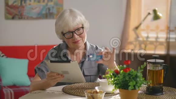 老年妇女在公寓里用平板电脑购物视频的预览图